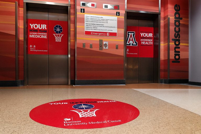 Elevator doors with custom red graphics promoting home health and medical services at Banner University Medical Center. Wall signage and floor graphic create a professional, branded healthcare environment.