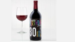 Colorful birthday wine bottle with custom label and glass of red wine against plain background, perfect for personalized event decorations and special occasion celebrations.