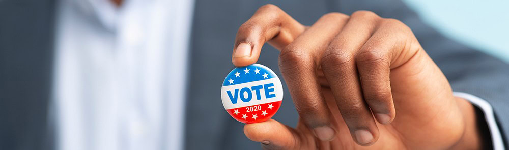 Voter holding a "VOTE 2020" campaign button, promoting election participation and civic engagement.