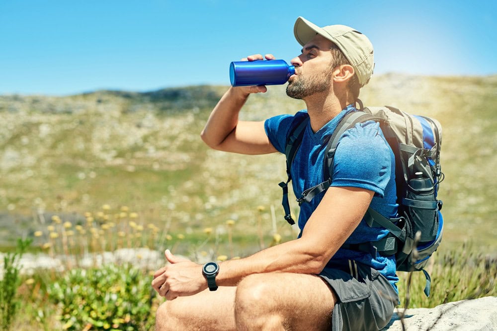 Refreshing outdoor scene of a man in hiking gear drinking water during a trail break in nature.