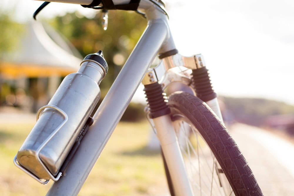 Aluminum water bottle attached to a bicycle frame with a scenic outdoor background.