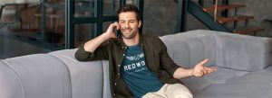 Relaxed man talking on cell phone while sitting on modern gray sofa in stylish indoor setting.