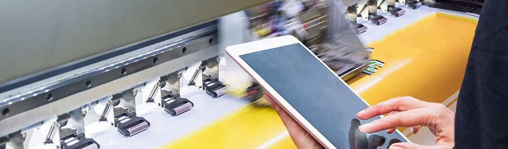 Digital signage printing process on a large format printer with a handheld device in a print shop, showcasing custom signage production.