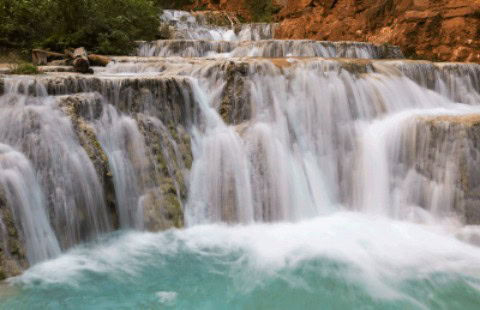 Vibrant waterfall cascading over rocks with lush greenery in the background, showcasing natural beauty and serene outdoor scenery.