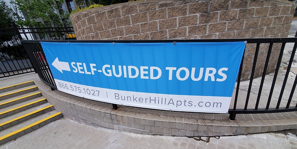 SELF-GUIDED TOURS banner with contact information and website for Bunker Hill Apartments, displayed on a metal fence near steps.