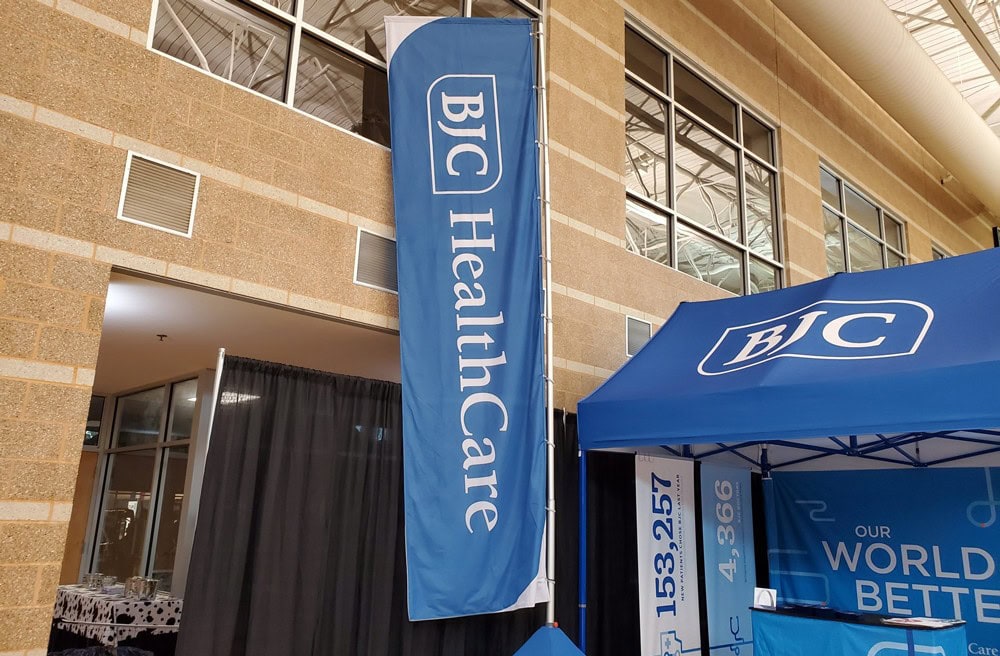 Feather Flag Design Tips - A Guide to Feather Flag Design 2 Bold blue banner and canopy with "BJC Healthcare" branding, promoting a healthcare organization at an event.