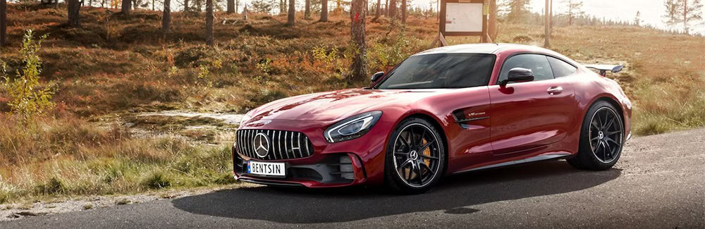 Luxury red sports car parked on scenic roadside in autumn landscape.