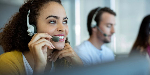 A smiling customer service representative wearing a headset in a modern call center setting.