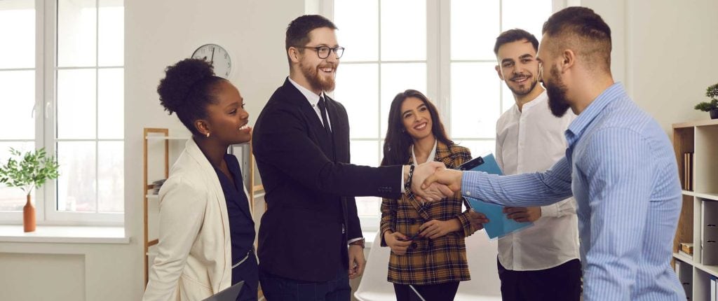 Graphic Impact Company Policies 1 Diverse professionals shaking hands in a modern office, showcasing teamwork and collaboration for business success.
