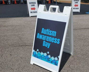 Vivid Autism Awareness Day outdoor sign promoting inclusion and support, featuring puzzle piece graphics and bold blue text on a white A-frame board.