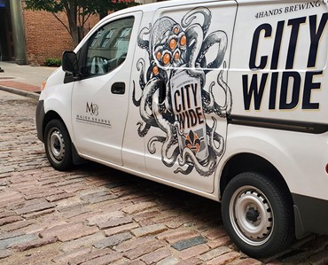 Vivid graphic of an octopus with city-wide text on a white delivery van, showcasing custom vehicle wraps by Graphic Impact.