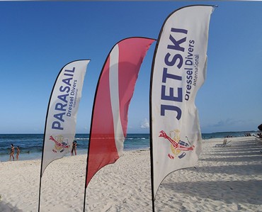 Vibrant beach flags with customizable logos and designs standing on sandy shores with ocean in background, ideal for promotional events and branding at outdoor locations.