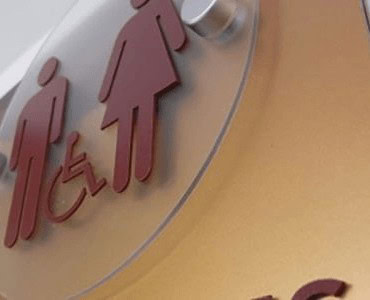 Red and pink restroom signs, including accessible symbol, mounted on a wall; professional signage design for public facilities.