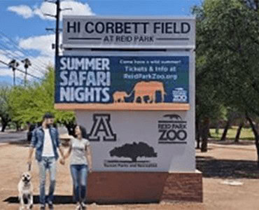 Hi corbett field sign at red park with people and trees in background.