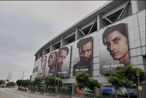 Vivid large banners for the movie "Old Guard" on a modern building facade with promotional posters featuring diverse characters.