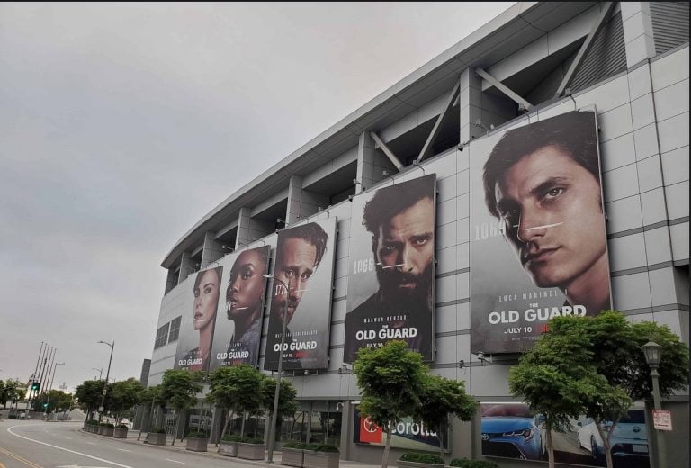 Vivid large banners for the movie "Old Guard" on a modern building facade with promotional posters featuring diverse characters.