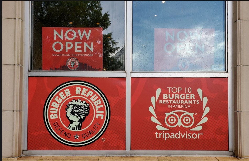 Now open signage and top 10 burger restaurants in America display on storefront window, featuring bright red promotional decals for local diner.