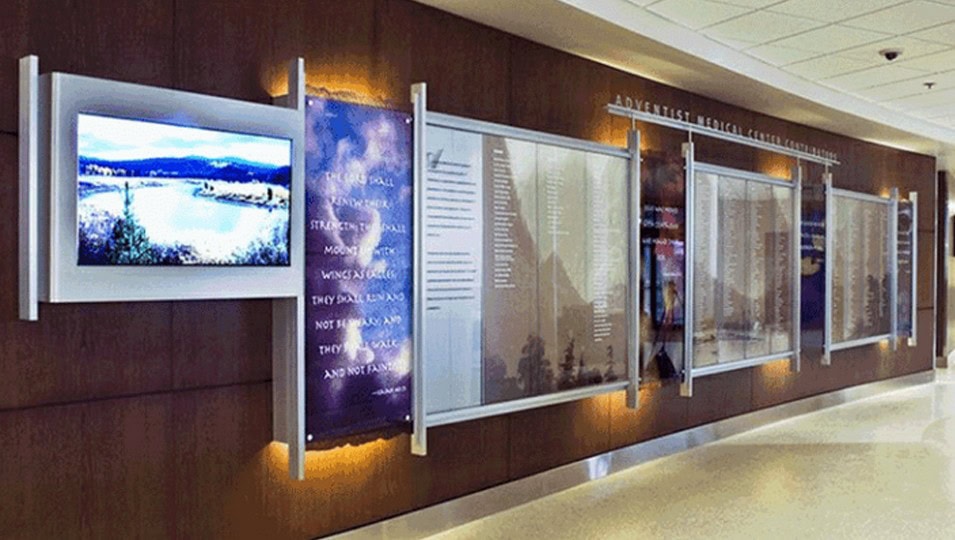 Full Color Backlit Signs 1 A digital display and glass-encased signage boards installed on a wooden wall within an indoor space, suitable for informational and advertising purposes.