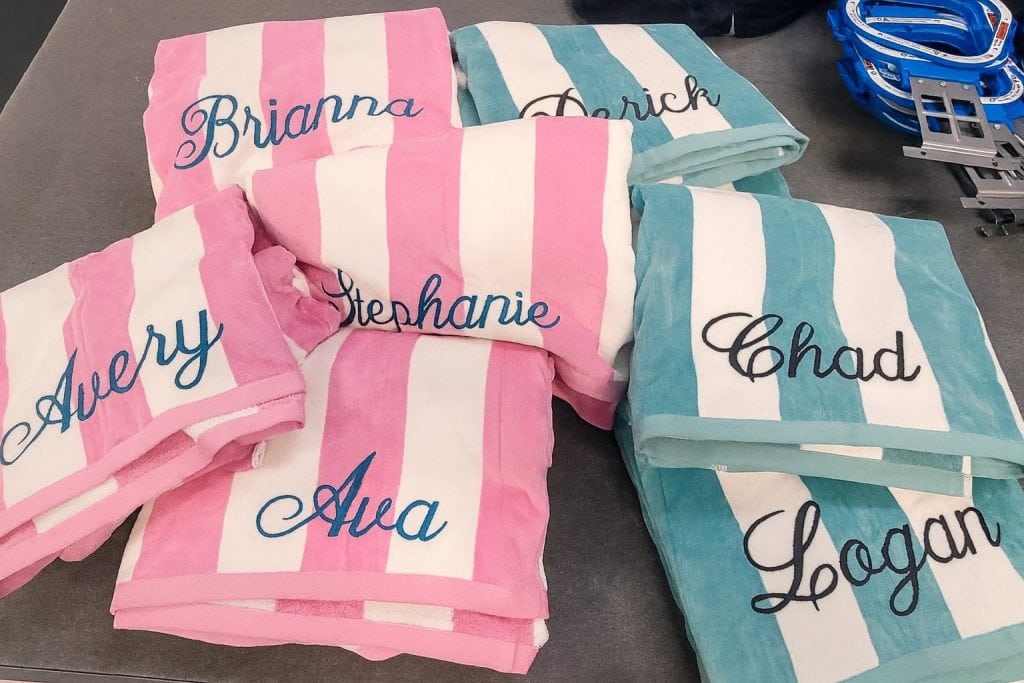 Custom embroidered towels with name and logo personalization, pink and teal striped towels for events, personalized towels for friends and family, high-quality embroidery on decorative towels for giveaways.