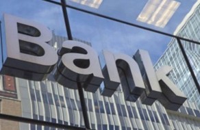 Bold 3D “Bank” signage on a glass storefront, reflecting nearby skyscrapers and cityscape, representing financial institution branding.