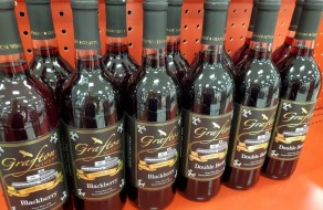– Bottles of blackberry-flavored wine with custom winery labels displayed on an orange shelf.