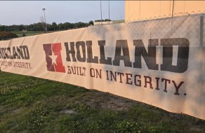 Large outdoor banner with “Holland Built on Integrity” slogan displayed along a sports field fence, illustrating custom signage and branding solutions offered by Graphic Impact.
