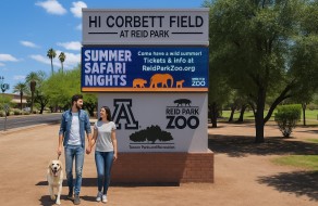 Colorful park signage promoting zoo events and recreational activities at Reid Park Zoo with visitors enjoying a sunny day outdoors.