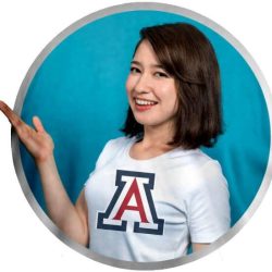 A woman smiling and pointing to her University of Arizona t-shirt, promoting custom signs, banners, engraving, and apparel at Graphic Impact.
